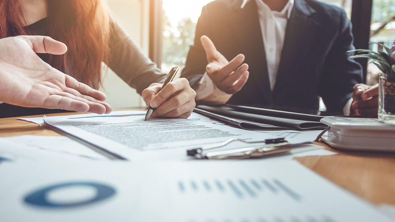 Close up of people sitting around table while one person signs a document Close up of people sitting around table while one person signs a document