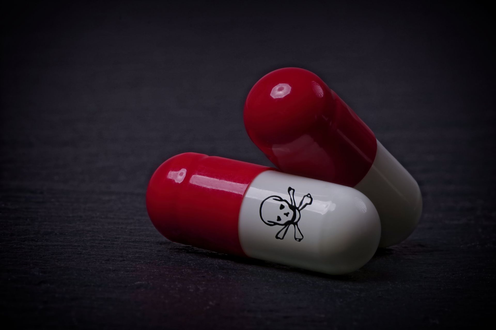 Drug capsules with skull and crossbone on dark stone background